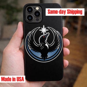 May include: Black phone case featuring a stylized bird design with a star above its head. The bird is black with a red eye, set against a white and blue circular background. The text "Made in USA" is visible.