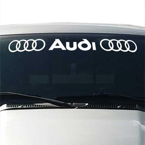Puede incluir: Calcomanía de vinilo blanco para coche con el logotipo y el nombre de Audi. El logotipo de Audi consta de cuatro anillos entrelazados. La palabra "Audi" está escrita en negrita, con una fuente sans-serif. Diseñado para ser aplicado en el parabrisas de un vehículo.