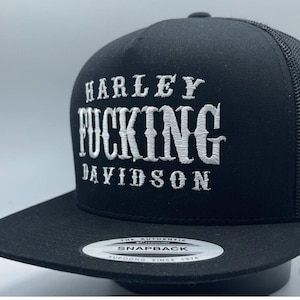 May include: Black snapback cap featuring white embroidered text: "HARLEY FUCKING DAVIDSON". The cap has a mesh back and a flat peak. A tag reads "THE AUTHENTIC SNAPBACK".