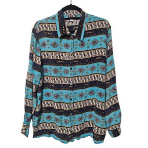 Może przedstawiać: Koszula zapinana na guziki z długim rękawem i kolorowym wzorem. Koszula ma turkusowe tło z granatowymi i złotymi akcentami. Wzór zawiera łańcuchy, gwiazdy i kształty geometryczne. Koszula wisi na czarnym wieszaku.