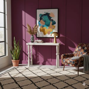 Puede incluir: Un salón con una consola blanca, un sillón estampado y una alfombra con diseño de rejilla negra. Una pintura abstracta enmarcada cuelga de una pared morada. Una lámpara dorada está sobre la mesa y se ve una planta en maceta.