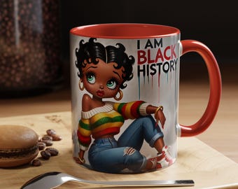 May include: A ceramic mug with a red interior and handle, featuring a cartoon illustration of a woman with the text "I AM BLACK HISTORY." The woman is wearing a striped sweater, ripped jeans, and red and white sneakers.