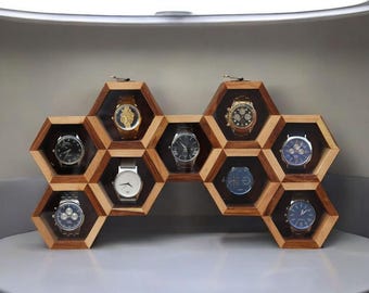 May include: A wooden honeycomb-shaped watch display case with nine compartments, each holding a wristwatch. The case is made of light brown wood and has a clear glass front for each watch. The watches have various colored faces and bands.