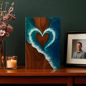 Peut inclure: Tableau mural en bois avec un motif en forme de cœur. Le cœur est formé par des vagues bleues et blanches sur un fond en bois marron. L'œuvre d'art porte les initiales "CZ" et les mots "Chalk Elixir" en bas.