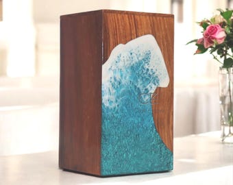 May include: A wooden box featuring a wave design in shades of blue and white. The wave has a textured, foamy appearance. The rectangular box is made of wood with a natural grain. The text "CZ" is visible on the wave design, which is a decorative element.