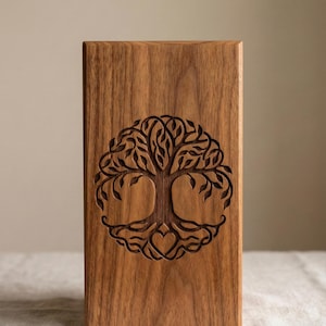 May include: A rectangular wooden box with a carved tree of life design. The tree features a heart at the base and is surrounded by a circular pattern of leaves. The wood has a warm, natural brown tone.