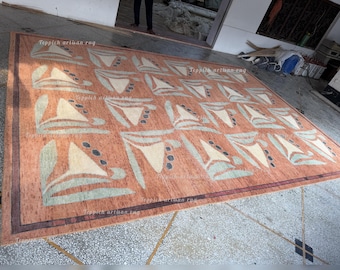 May include: A large rectangular area rug featuring a terracotta orange background with a repeating grid pattern of cream-colored triangular shapes, sage green leaf-like accents, and small dark gray circles, bordered by a dark brown frame.