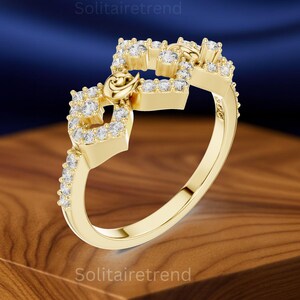 Puede incluir: Un anillo dorado con un dise&ntilde;o &uacute;nico. El anillo presenta una serie de formas cuadradas adornadas con peque&ntilde;as piedras preciosas transparentes. Un peque&ntilde;o elemento decorativo est&aacute; centrado en el anillo. El anillo se muestra sobre una superficie de madera.