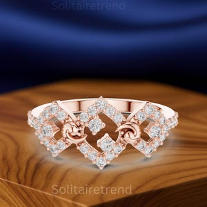 Puede incluir: Anillo de oro rosa con un dise&ntilde;o geom&eacute;trico, con m&uacute;ltiples piedras preciosas redondas y transparentes. El anillo tiene una forma &uacute;nica con espacios abiertos y elementos decorativos.
