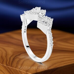 Puede incluir: Un anillo plateado con un dise&ntilde;o &uacute;nico, con m&uacute;ltiples grupos de peque&ntilde;as piedras preciosas transparentes. La banda del anillo tambi&eacute;n est&aacute; adornada con piedras preciosas m&aacute;s peque&ntilde;as. El anillo se muestra sobre una superficie de madera con un fondo azul.