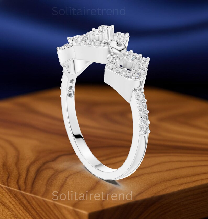 Puede incluir: Un anillo plateado con un dise&ntilde;o &uacute;nico, con m&uacute;ltiples grupos de peque&ntilde;as piedras preciosas transparentes. La banda del anillo tambi&eacute;n est&aacute; adornada con piedras preciosas m&aacute;s peque&ntilde;as. El anillo se muestra sobre una superficie de madera con un fondo azul.
