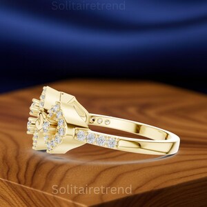 Puede incluir: Un anillo dorado con un grupo de peque&ntilde;as piedras preciosas transparentes. El anillo presenta un dise&ntilde;o floral con una banda de piedras m&aacute;s peque&ntilde;as. El anillo se exhibe sobre una superficie de madera.