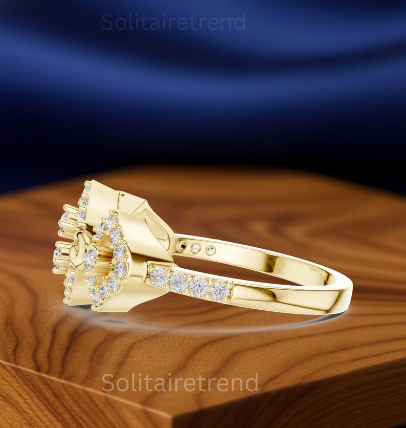 Puede incluir: Un anillo dorado con un grupo de peque&ntilde;as piedras preciosas transparentes. El anillo presenta un dise&ntilde;o floral con una banda de piedras m&aacute;s peque&ntilde;as. El anillo se exhibe sobre una superficie de madera.