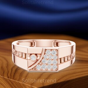 May include: Rose gold ring with a geometric design. The ring features a square cluster of small, clear stones and a single, round stone. The band has a rectangular shape with linear detailing. The text "Solitairetrend" is visible.