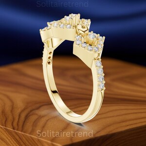 Puede incluir: Un anillo dorado con un dise&ntilde;o &uacute;nico, con m&uacute;ltiples piedras preciosas transparentes. El anillo tiene una ca&ntilde;a dividida y una parte superior decorativa con un elemento en forma de coraz&oacute;n. El anillo est&aacute; sobre una superficie de madera.
