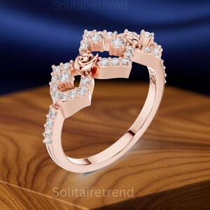 Puede incluir: Anillo de oro rosa con un dise&ntilde;o &uacute;nico. El anillo presenta una serie de formas cuadradas adornadas con peque&ntilde;as piedras claras y brillantes. Un delicado detalle en forma de coraz&oacute;n est&aacute; incorporado, agregando un toque de elegancia. El anillo est&aacute; sobre un fondo borroso.