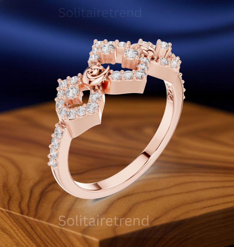 Puede incluir: Anillo de oro rosa con un dise&ntilde;o &uacute;nico. El anillo presenta una serie de formas cuadradas adornadas con peque&ntilde;as piedras claras y brillantes. Un delicado detalle en forma de coraz&oacute;n est&aacute; incorporado, agregando un toque de elegancia. El anillo est&aacute; sobre un fondo borroso.