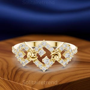 Puede incluir: Un anillo dorado con un dise&ntilde;o de diamantes. El anillo presenta una forma cuadrada central con diamantes y elementos curvos a cada lado. El anillo est&aacute; sobre una superficie de madera.
