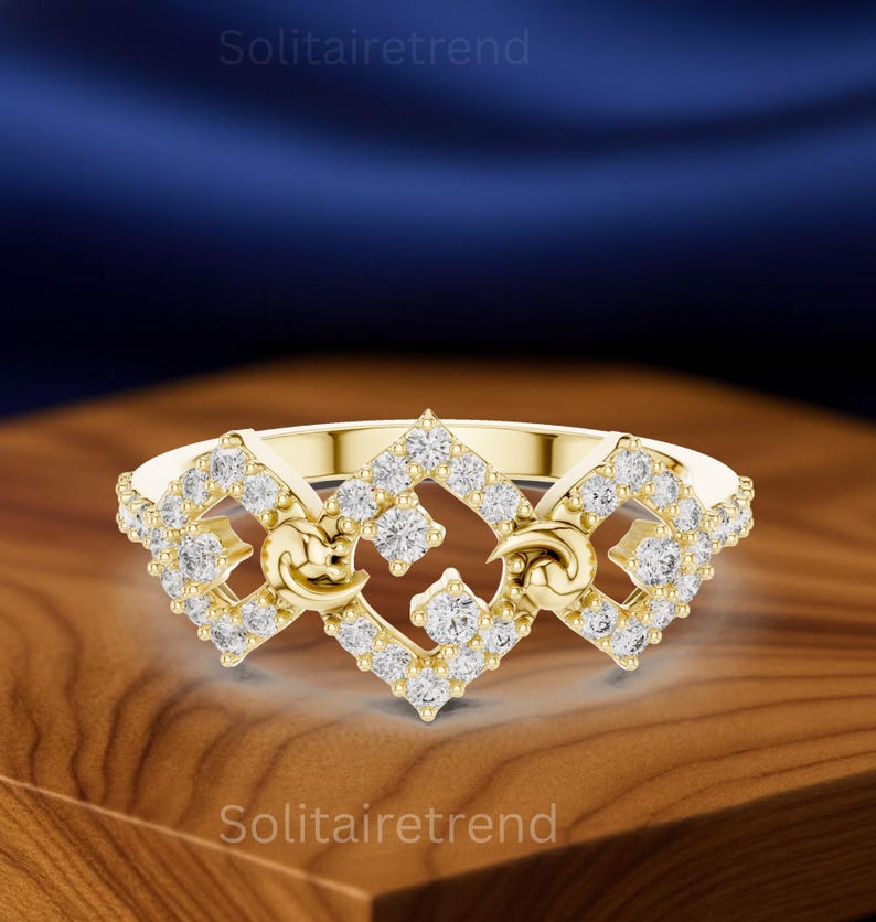 Puede incluir: Un anillo dorado con un dise&ntilde;o de diamantes. El anillo presenta una forma cuadrada central con diamantes y elementos curvos a cada lado. El anillo est&aacute; sobre una superficie de madera.