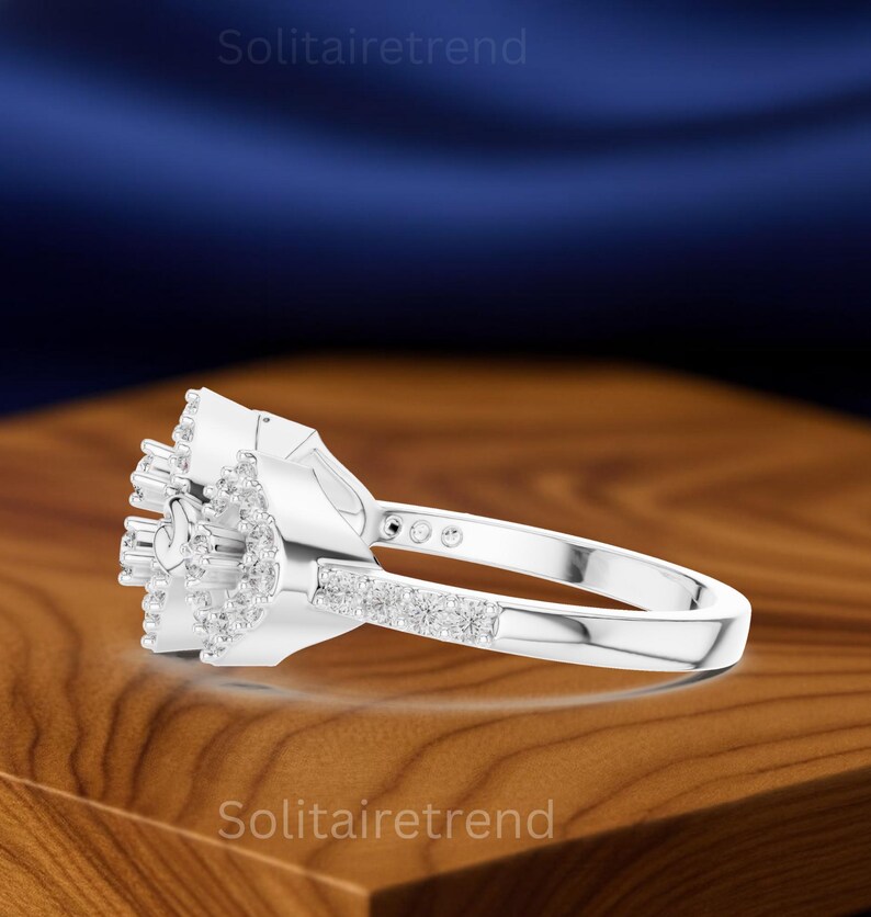 Puede incluir: Un anillo de plata con un grupo de peque&ntilde;as piedras transparentes en un dise&ntilde;o floral. La banda presenta una fila de peque&ntilde;as piedras. El anillo se muestra sobre una superficie de madera con el texto "Solitairetrend".
