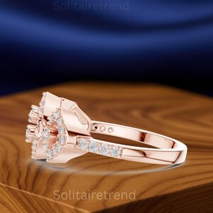 Puede incluir: Anillo de oro rosa con dise&ntilde;o floral, con m&uacute;ltiples piedras preciosas peque&ntilde;as y transparentes. La banda del anillo es lisa y el engaste muestra un grupo de piedras. El nombre de la marca "Solitairetrend" es visible.