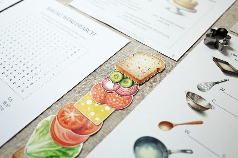 Puede incluir: Ilustraciones de papel de ingredientes para s&aacute;ndwiches, incluyendo pan, lechuga, tomate, queso, salami, pepino y cebolla roja. Tambi&eacute;n hay art&iacute;culos relacionados con la reposter&iacute;a, como un batidor, un colador y una sart&eacute;n, junto con un juego de b&uacute;squeda de palabras.