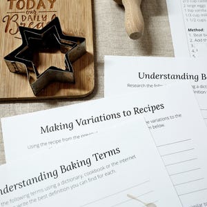 Puede incluir: Una tabla de cortar de madera con el texto "TODAY our DAILY Bread" y un cortador de galletas en forma de estrella. Tambi&eacute;n se ven hojas de trabajo de recetas y t&eacute;rminos de horneado.