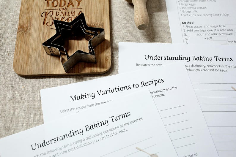 Puede incluir: Una tabla de cortar de madera con el texto "TODAY our DAILY Bread" y un cortador de galletas en forma de estrella. Tambi&eacute;n se ven hojas de trabajo de recetas y t&eacute;rminos de horneado.