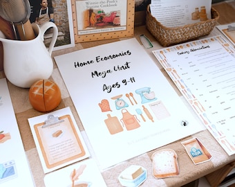 Puede incluir: Materiales educativos para economía doméstica, incluyendo un cuaderno de trabajo titulado "Home Economics Mega Unit Ages 9-11", un libro de cocina y una tabla de abreviaturas de cocina. La imagen también presenta una jarra blanca y un panecillo naranja decorativo.