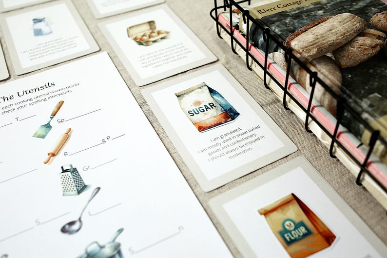 Puede incluir: Un conjunto de tarjetas ilustradas y una hoja de trabajo relacionadas con la reposter&iacute;a. Las tarjetas presentan im&aacute;genes de acuarela de ingredientes como az&uacute;car y harina, con texto descriptivo. Una cesta de alambre contiene libros y una hoja de trabajo muestra utensilios de cocina.