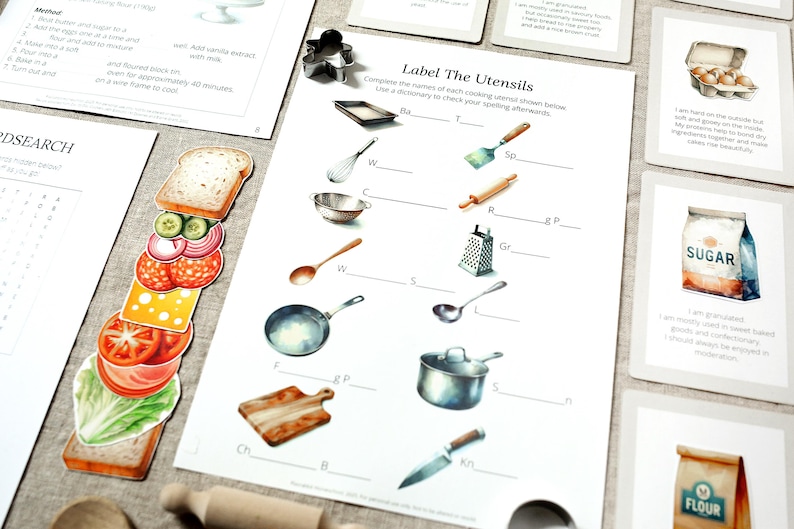 Puede incluir: Material educativo con tem&aacute;tica de cocina. Incluye una hoja de trabajo titulada "Label The Utensils" con ilustraciones de utensilios de cocina, tarjetas de recetas y un marcap&aacute;ginas con forma de s&aacute;ndwich. Ilustraciones de estilo acuarela.