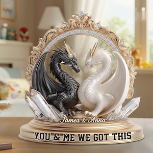 May include: A gold-toned decorative sculpture featuring two dragons facing each other within a decorative frame. One dragon is black, the other white. The base reads "YOU & ME WE GOT THIS" with the names "James & Anna".