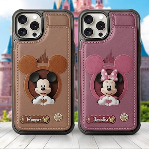 May include: Two phone cases featuring Mickey and Minnie Mouse. One case is brown with a Mickey Mouse design, the other is pink with a Minnie Mouse design. Both cases have a card slot and the names "Robert" and "Jessica" are printed on them.