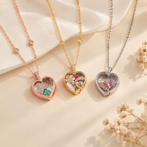May include: Three heart-shaped locket necklaces in rose gold, yellow gold, and silver tones. Each locket features a clear glass front containing small decorative charms, including flowers and a butterfly, suspended on delicate matching metal chains.