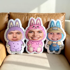 May include: Three bunny-shaped plush cushions with faces. One is purple, one is pink, and one is blue. The cushions are on a brown leather sofa. The cushions have bunny ears and are in the shape of a bunny costume.
