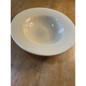 May include: A white ceramic bowl with a slightly rippled surface. The bowl is shallow and has a wide rim.