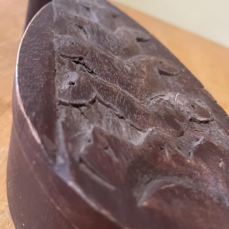 May include: Close-up of a carved wooden object with a dark brown finish. The wood has a textured surface with visible grain and intricate carvings. The object appears to be part of a larger piece, possibly a decorative element.