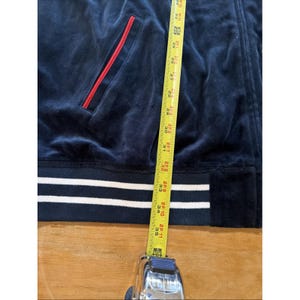 May include: Navy blue velour zip-up jacket with a red-lined pocket and white stripes at the hem. The jacket is measured with a tape measure, showing a length of approximately 35 inches.