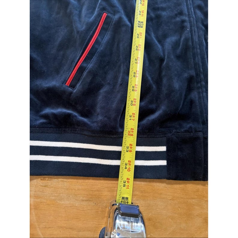 May include: Navy blue velour zip-up jacket with a red-lined pocket and white stripes at the hem. The jacket is measured with a tape measure, showing a length of approximately 35 inches.