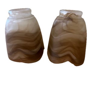 May include: Two decorative glass light shades with a unique, swirled brown and white pattern. The shades have a rounded, bell-like shape with a slightly flared top. The glass has a translucent quality, allowing light to pass through.