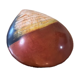 May include: A smooth, teardrop-shaped decorative object featuring a polished finish. The surface displays a color gradient transitioning from a deep, solid black on the left to a warm, earthy reddish-brown, accented by a textured, wood-grain pattern.
