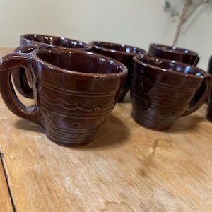 May include: Set of six brown ceramic mugs with a wavy design. The mugs have a handle and are perfect for coffee or tea.