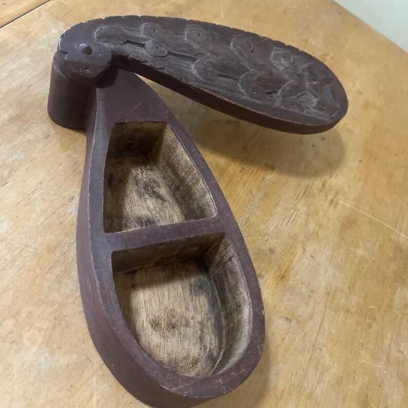 May include: A handcrafted wooden box with a hinged lid. The box is a teardrop shape with two interior compartments. The lid is decorated with carved floral designs. The box is stained a dark reddish-brown color.