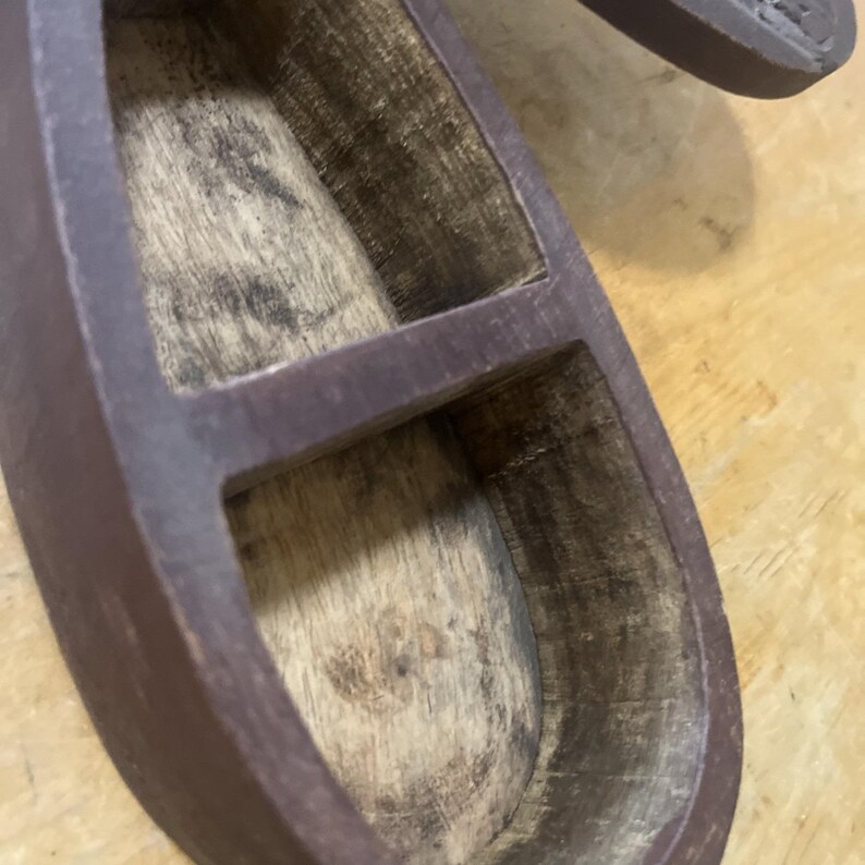 May include: A close-up of a wooden, two-compartment container. The container is a dark brown color with a natural wood interior. The compartments are separated by a divider. The container is on a light brown surface.