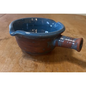 May include: A blue and red ceramic serving bowl with a handle. The bowl has a blue glaze on the inside and a red glaze on the outside.