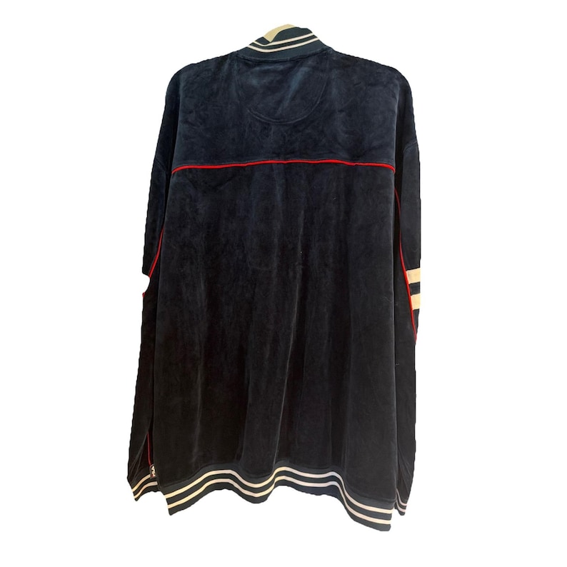 May include: Navy blue velour zip-up jacket with red and white accents. The jacket features a white and navy striped collar and cuffs. The back of the jacket has a red stripe across the upper back and white stripes down the sleeves.