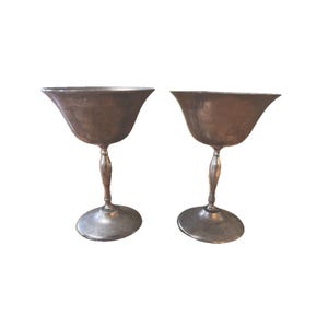 May include: Two silver goblets with a wide bowl and a tall, slender stem. The goblets are made of a shiny metal and have a classic design.