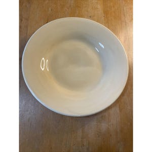 May include: A white ceramic bowl with a smooth, rounded rim. The bowl is empty and has a slight sheen.
