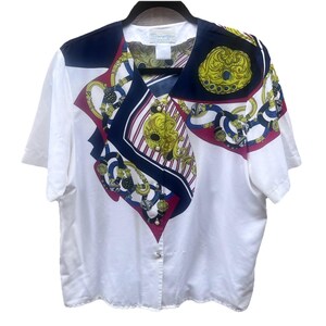 Könnte beinhalten: Weißes Kurzarm-Bluse mit einem dekorativen schalartigen Einsatz. Der Einsatz zeigt ein marineblaues, rotes und goldenes Muster mit Ketten- und Medaillondesign. Die Bluse hat einen V-Ausschnitt und einen Knopfverschluss.