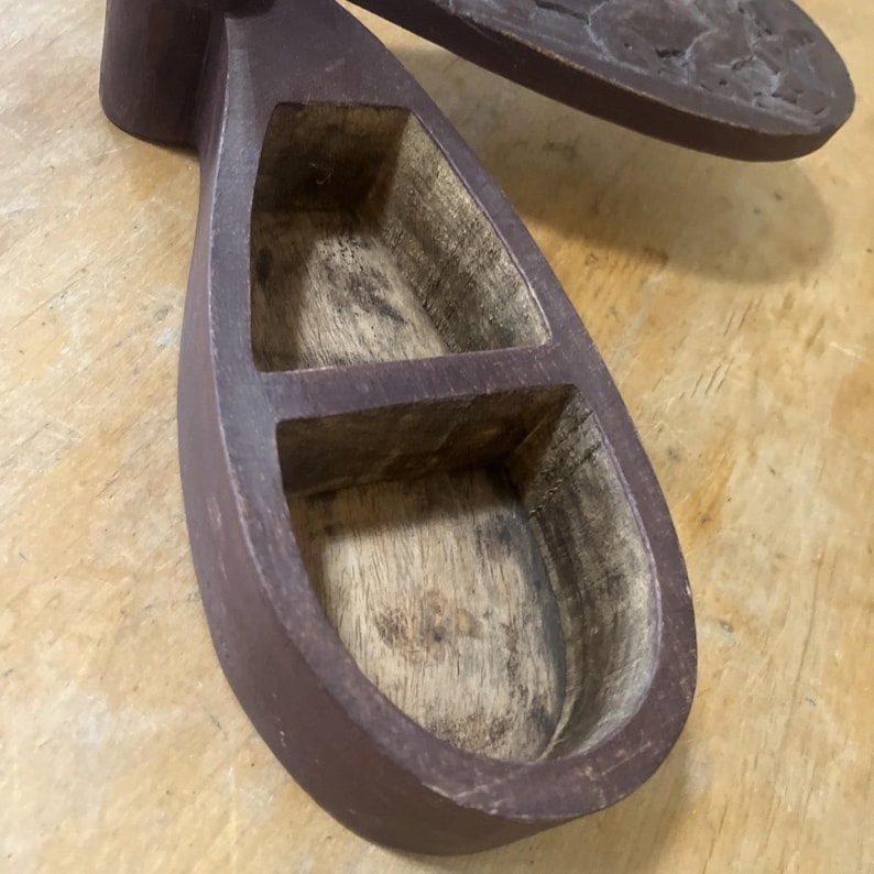 May include: A handcrafted, wooden spice rack with a dark brown finish. The rack features two compartments and a separate, oval-shaped lid. The interior of the rack shows the natural wood grain.
